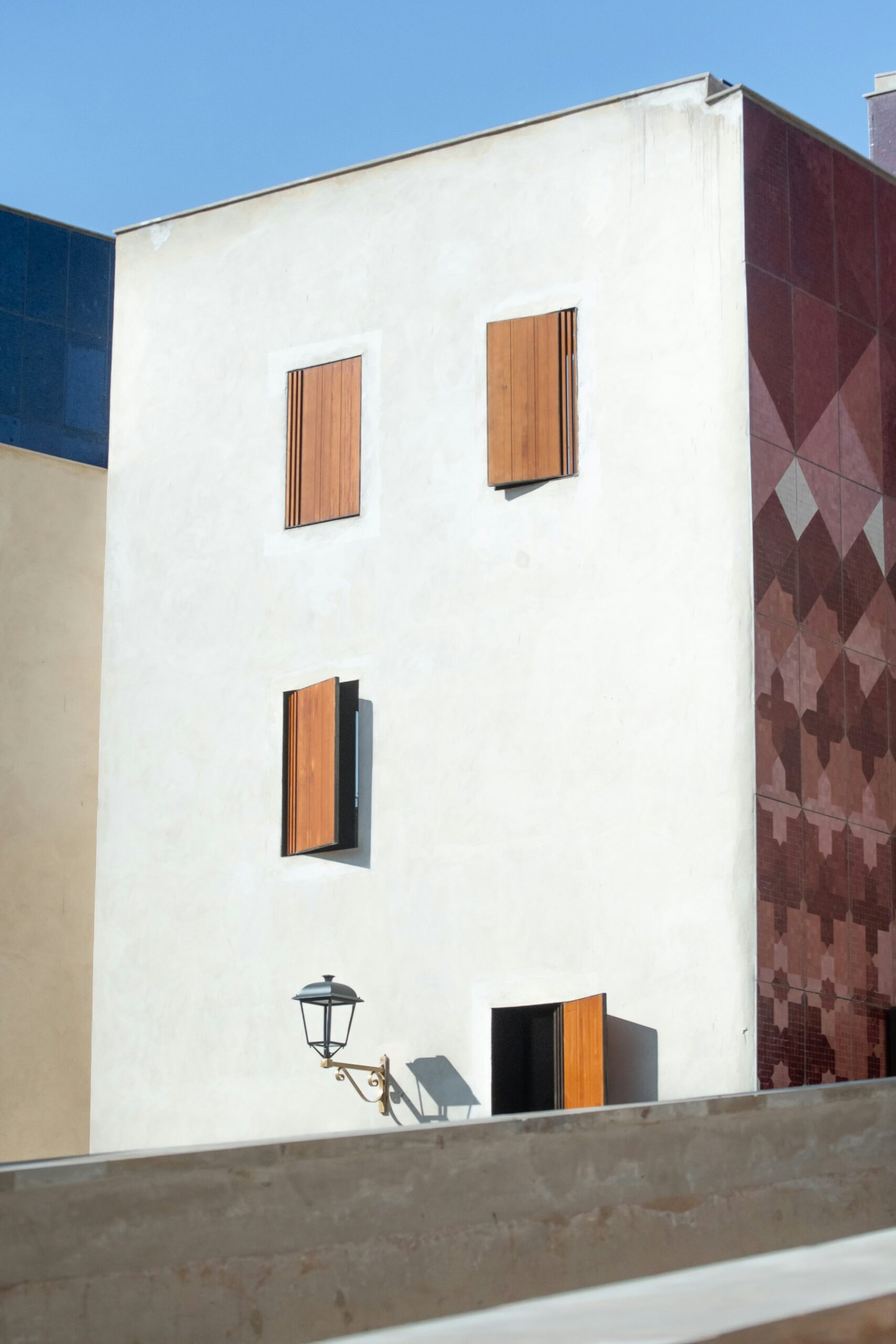 A white Moroccan wall with wooden shutters and geometric tile detail.